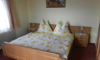 A simple guest room with a double bed and two nightstands. The walls are in neutral colors, and a picture of landscapes hangs above the bed.