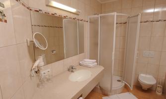 A modern bathroom with a shower cabin and a sink. Clean towels are ready, and the walls are brightly tiled.