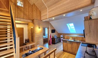 A bright and modern wooden house with an open kitchen and dining area. The wooden staircase leads to another area on the upper floor.