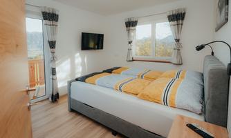 A cozy bedroom with a double bed and modern furniture. Large windows offer a view outside and let in plenty of daylight.