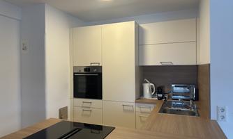 A modern kitchen with a smooth countertop and high-quality appliances. The furniture is in light colors, creating an open and inviting space.