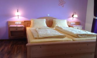 A cozy bedroom with a double bed and yellow bedding. The walls are painted purple, and there are nightstands with lamps.