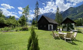 A beautiful garden with two wooden huts and a view of the mountains. The sky is blue and the clouds are white.