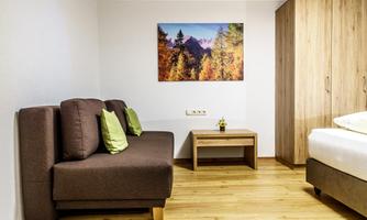 A cozy room with a brown sofa, two cushions, and a wooden table. On the wall hangs a picture of an autumn landscape.