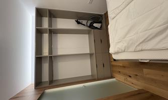 A modern room with a large wardrobe and a bed. In the background, there is a vacuum cleaner.