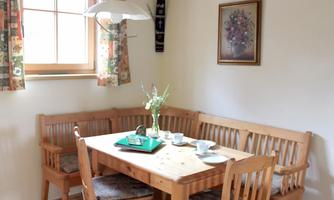 A cozy dining area with a wooden house and a round table. On the table are dishes and a bouquet in a vase.