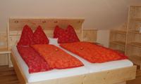 A cozy bedroom with a large wooden bed and colorful blankets. The walls are bright and the floors are made of wood, creating a warm atmosphere.