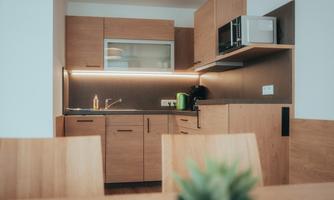A modern kitchen with wooden cabinets and a cooking area. It is well equipped with a refrigerator, microwave, and a sink.