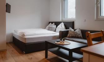 A cozy room with a double bed and a sofa bed. The room is bright and modernly designed with a table and a TV on the wall.