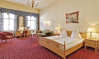 A spacious room with a double bed, an armchair, and a sofa. The walls are in warm colors, and there are large windows with curtains.