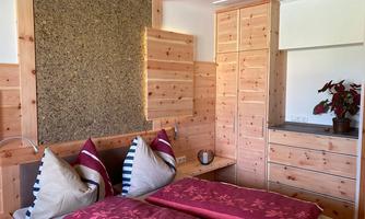 A cozy room with two beds and wooden furniture. The walls are paneled with wood, and a plant is on the dresser.