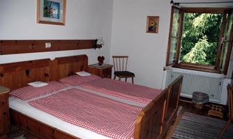 A cozy bedroom with a double bed and checkered bedspreads. A window offers a view of nature and the room has wooden interiors.