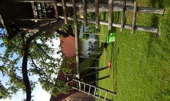 An outdoor playground with a tree height and a seesaw. In the background, there is a wooden hut and green grass.