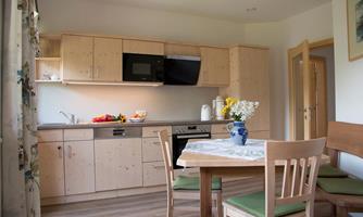 A bright kitchen with wooden cabinets and a table with chairs. Fresh fruit and a vase of flowers are on the countertop.