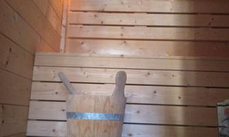 A relaxing sauna area made of wood with a cozy bench and a wooden vessel. The warm lights create a pleasant atmosphere.