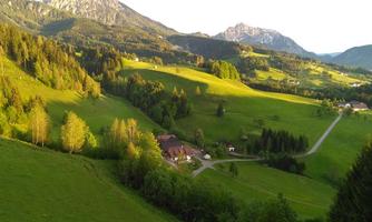 A tranquil landscape with gentle hills and vast greenery. In the background, there are mountains and a small village.