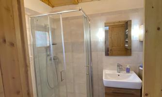 A modern bathroom with a shower, a sink, and a wooden ceiling. The room has bright tiles and a friendly atmosphere.