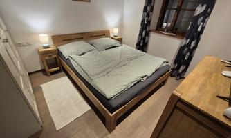 A cozy bedroom with a wooden bed and a soft blanket. The room has a window and warm light from the bedside lamps.