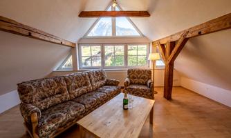 A cozy living space with a comfortable couch and an armchair. Large windows provide a view of the landscape.