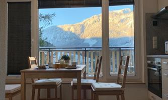 A cozy dining area with a table and chairs. In the background, snow-covered mountains and a blue sky are visible.