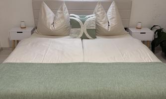 A modern bedroom with a double bed and light cushions. Next to the bed, there are two bedside lamps on small nightstands.