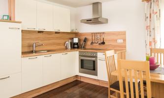 A modern kitchen with white cabinets and wooden elements. A table with chairs is located next to the cooking area.