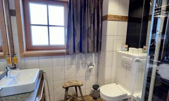 A modern bathroom with a shower and toilet. It features wood and tile elements as well as a window for natural light.