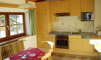 A cozy kitchen with modern appliances and wooden paneling. A dining area with a round table and chairs complements the friendly atmosphere.