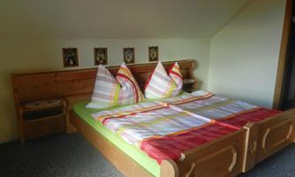 A cozy bedroom with a double bed and colorful pillows. Pictures hang on the wall, and the floor is carpeted.
