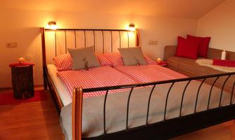 A cozy bedroom with a large double bed and checkered blankets. A seating area next to the bed complements the warm atmosphere.