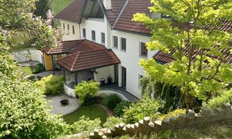 A beautiful house with a red roof surrounded by green trees and bushes. The well-kept garden invites relaxation.