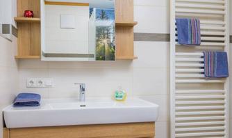 A modern bathroom with a wooden sink and a large mirror. A towel warmer with several towels hangs on the wall.