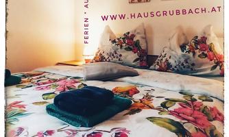 A cozy bedroom with a colorful bedspread and decorative cushions. Colorful pictures hang on the wall, enhancing the ambiance.