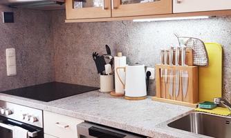 A modern kitchen with white cabinets and a granite countertop. On the countertop, there are kitchen utensils and a kettle.