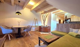 A cozy living space with a wooden beam ceiling and warm colors. There is a dining area and a lounge corner with comfortable armchairs and a warm atmosphere.