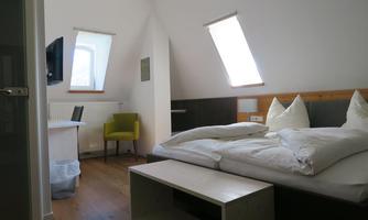A bright room with two beds, a desk, and a green chair. There are windows that let in natural light.