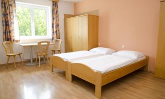 A simple room with two single beds and a table with chairs. The walls are peach-colored and the window offers a view outside.