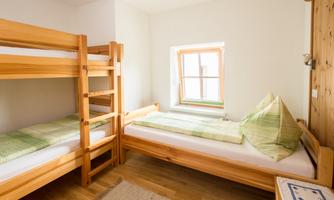 A simple, bright room with a bunk bed and a single bed. The beds are adorned with green bedding and pillows.