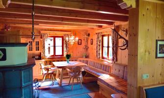 A cozy room with wooden walls and a large dining table. Light-filled windows and traditional decoration create a warm atmosphere.