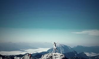 An impressive mountain landscape with two people on a summit. The sky is clear and the view extends over the clouds.
