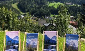Four deck chairs are positioned in a green garden with a mountain landscape in the background. The chairs feature impressive mountain motifs and invite relaxation.