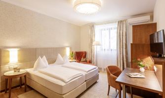 A cozy hotel room with a double bed and a desk. The room has plenty of daylight and a modern decor.