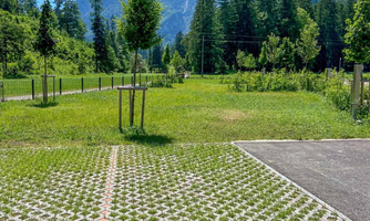 A green landscape with trees and mountains in the background. The paved area in the foreground features a beautiful, eco-friendly design.