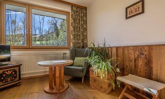 A cozy living area with a round table and a green armchair. The window offers a view of nature outside.