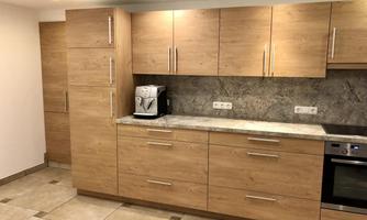 A modern kitchen with wooden fronts and a marble counter. The appliances are elegantly integrated and there is ample storage space.