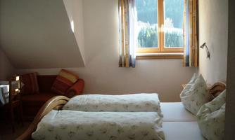 A cozy bedroom with two single beds and a window that lets in daylight. A seating area with a table complements the room.
