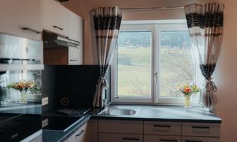 A modern kitchen with bright cabinets and a countertop. The window offers a view of a green landscape.