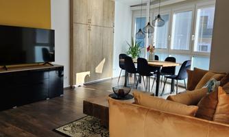 A modern living room with an orange sofa and a large TV. The dining area is bright and inviting, with a table and chairs.