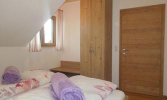 A cozy bedroom with two beds and pink towels. The room features wooden details and a window overlooking nature.