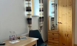 A simple room with a wooden table, a chair, and a wardrobe. Bright curtains let in light and create a friendly atmosphere in the space.